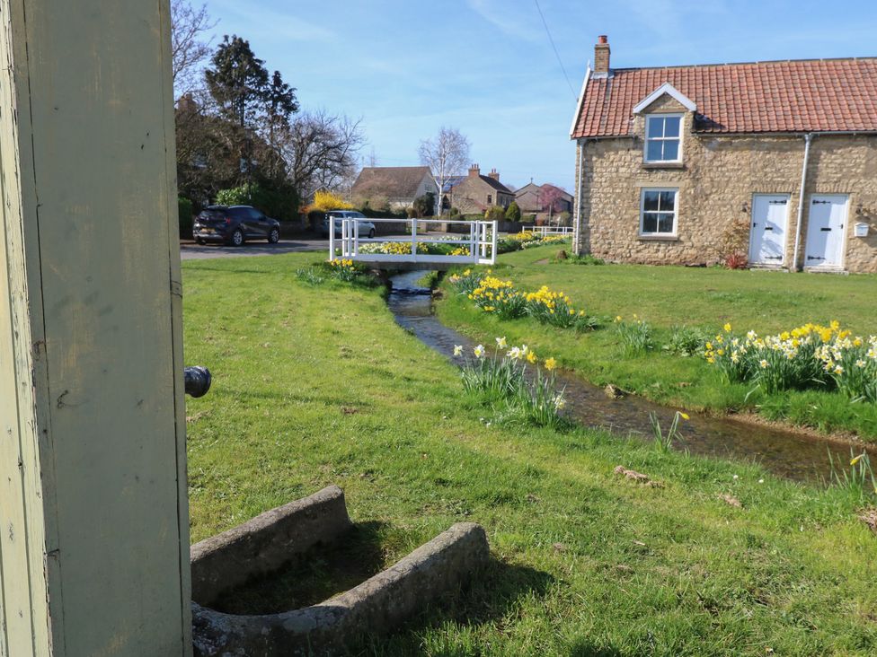 An outdoor area with a house, bridge over a stream, and flowers at Parr Cottage Snape near Bedale