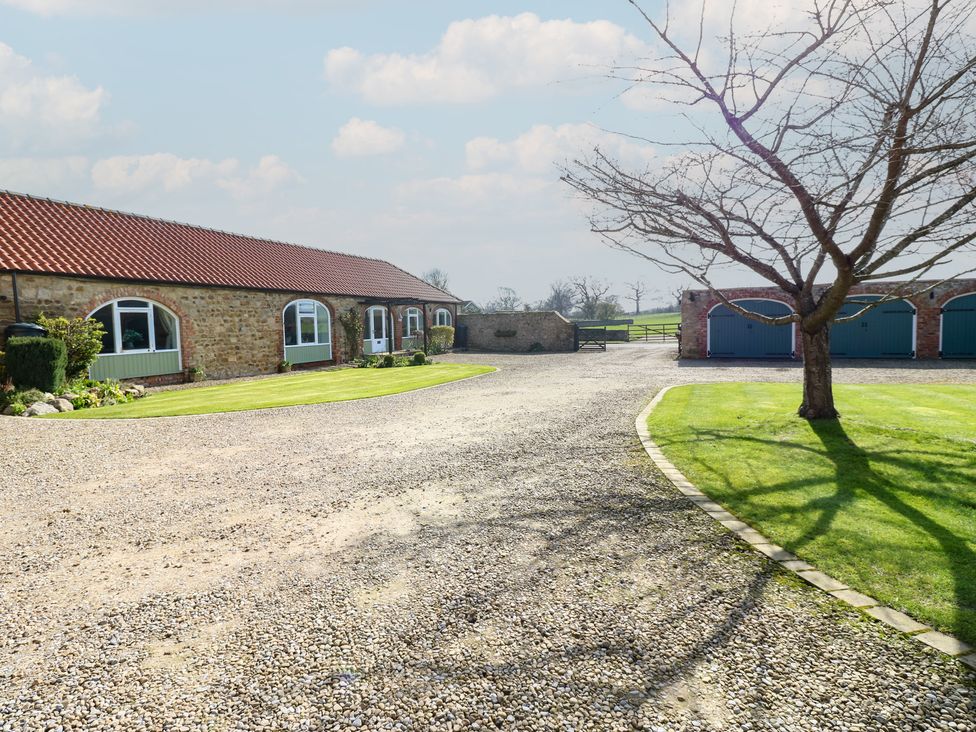 An outdoor view of a house and garage with a tree and gravel path at The Cart House in Snape near Bedale