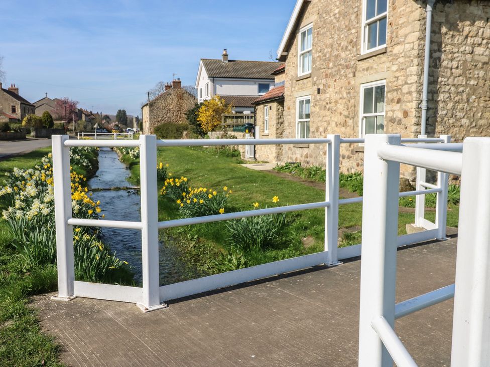 A railing overlooking a stream with daffodils at a property in Snape near Bedale