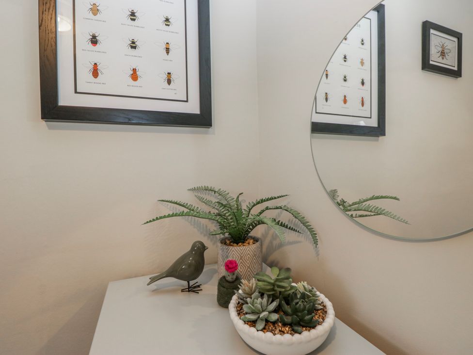 A bathroom corner with a mirror, framed print, and plant at The Thistles in Bowness-On-Windermere
