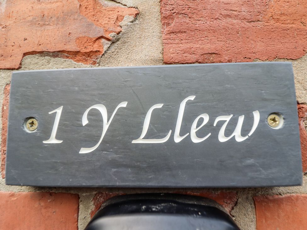 A slate sign with the text 1 Y Llew on a brick wall at 1 Y Llew in Llandinam