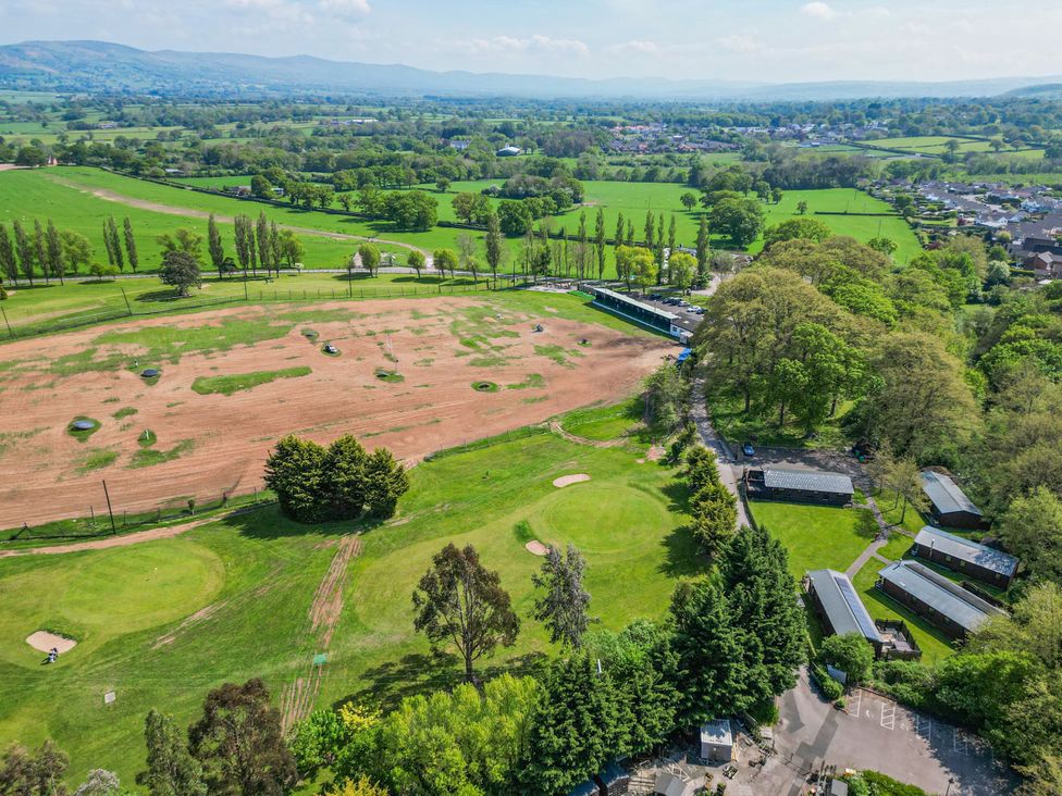 A golf course driving range and green areas with trees and buildings at The Blacktail in Llanerch Park near St Asaph