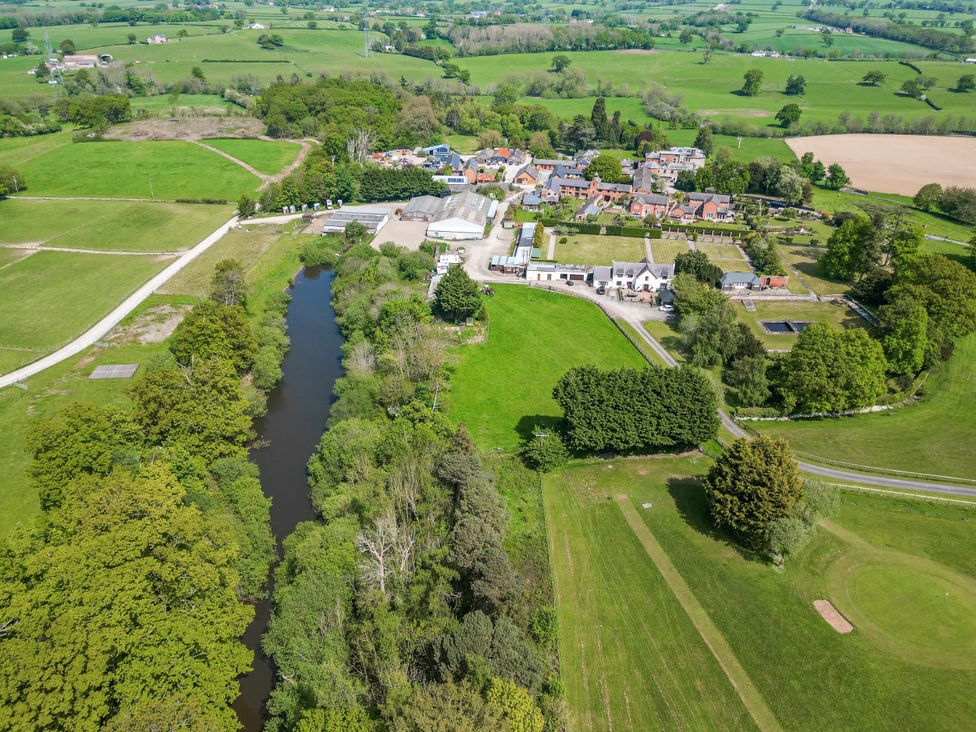 An aerial view of a countryside village with buildings trees and a river at The Blacktail in Llanerch Park near St Asaph