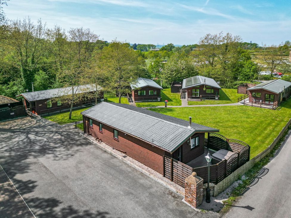 Several wooden cabins on a grassy area with trees and paved roads at The Blacktail in Llanerch Park near St Asaph