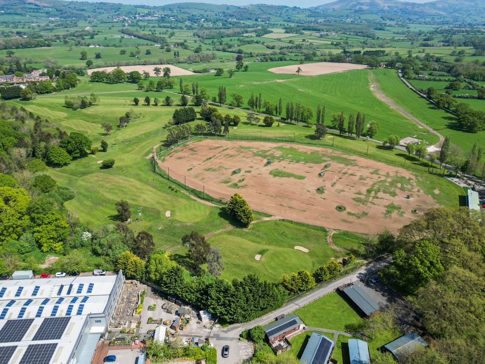 An aerial view of a golf course with a driving range a parking area and surrounding fields at The Buck in Llanerch Park near St Asaph