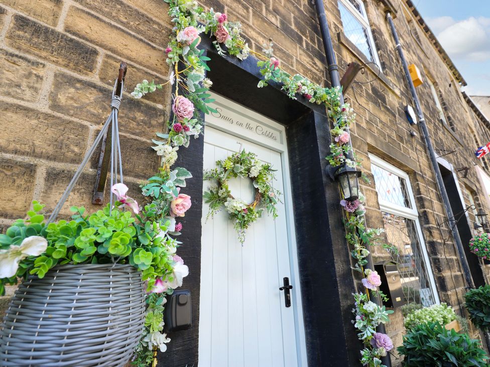 A flower-adorned front entrance with a white door at The Snug on the Cobbles, Haworth