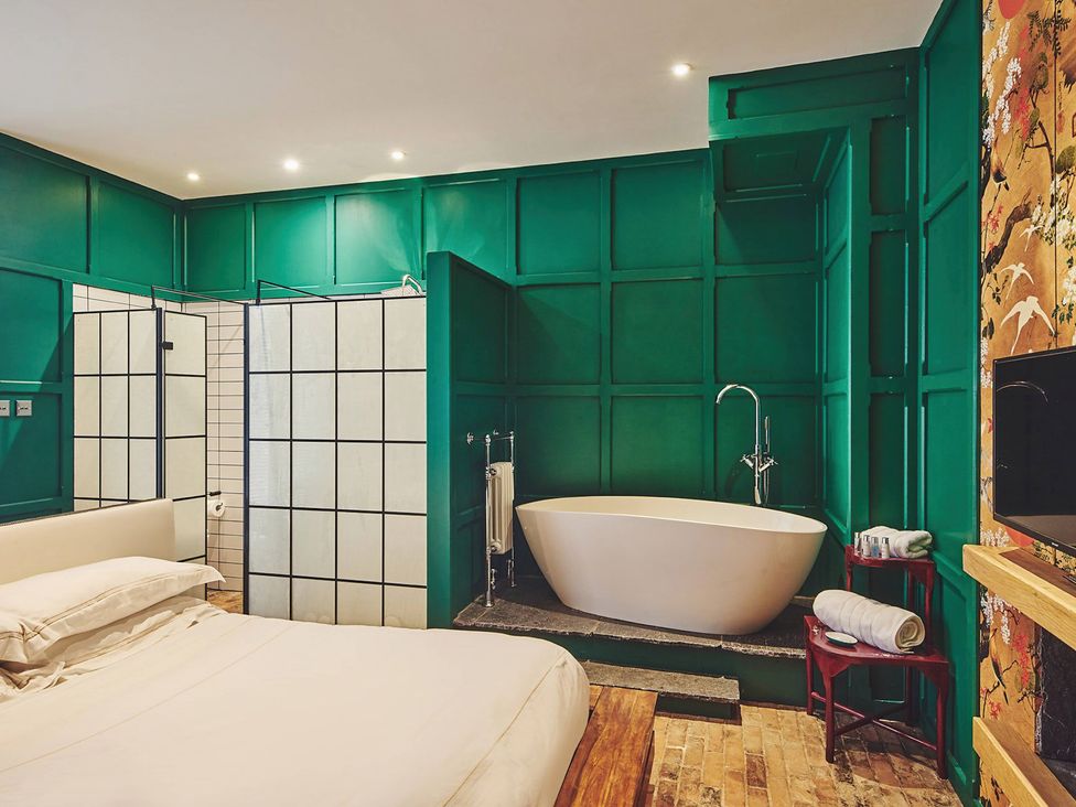 A bathroom with a bathtub and shower near a bed at The Carriages St Athan