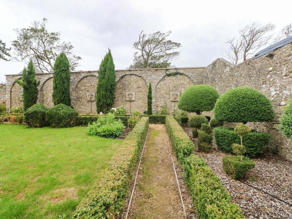 A garden with trimmed bushes and a stone wall at The Carriages in St Athan