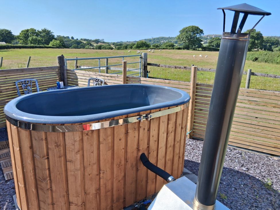 A hot tub with a chimney and chairs at Cwtch Winnie Shepherds Hut Old Colwyn