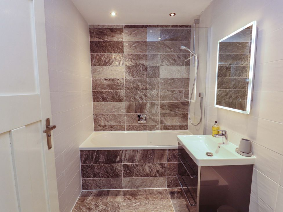 A bathroom with a bathtub, shower, sink, and mirror at Deer Wood At Applethwaite Hall in Windermere