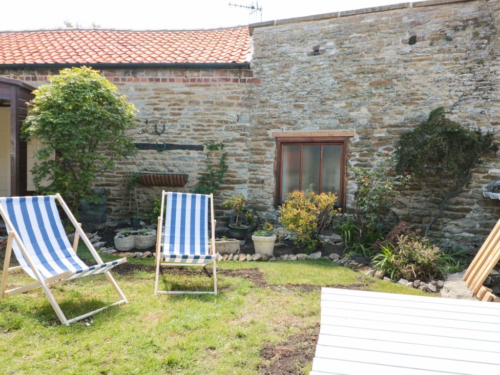 A garden with deck chairs and a stone wall at Rose Cottage East Ayton