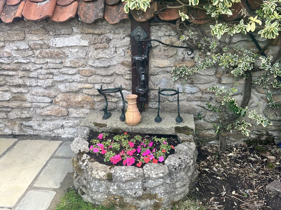A flower planter with a water pump and stone wall at Rose Cottage East Ayton