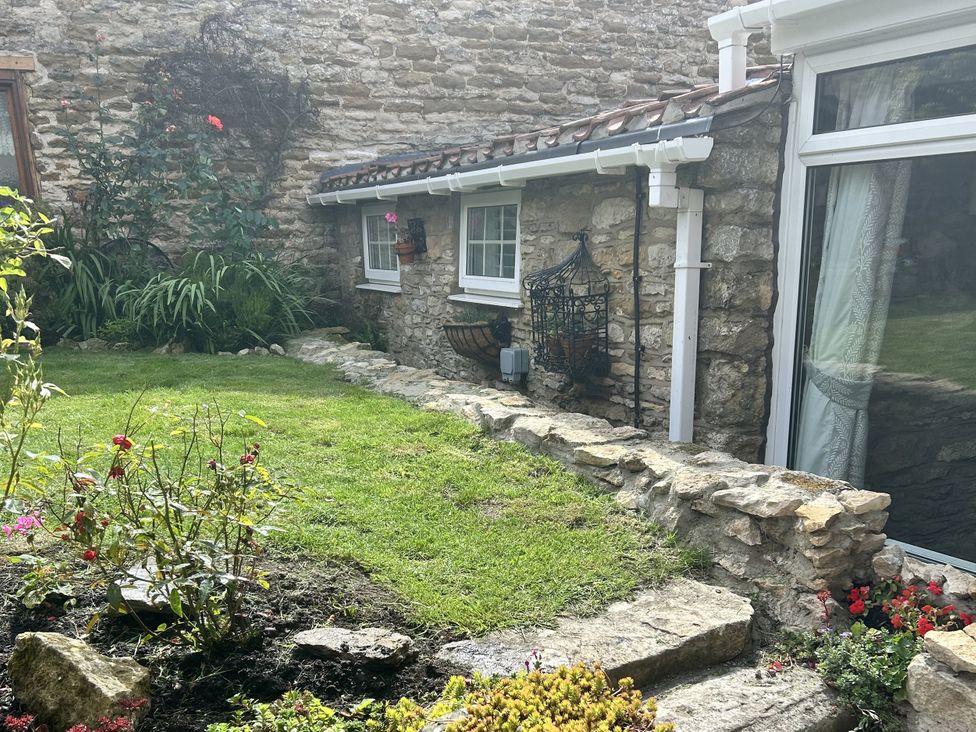 A garden with a stone wall and flower beds at Rose Cottage in East Ayton