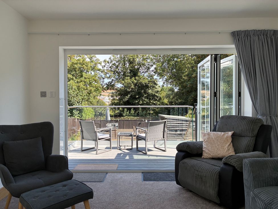 A living room with armchair and sofa leading to a patio at The Swanage Rail Lookout in Swanage