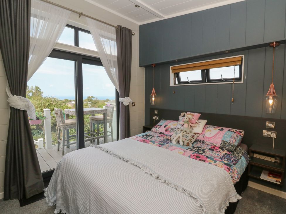 A bedroom with a bed and sliding door to an outdoor seating area at Coogee View in Maenygroes near New Quay