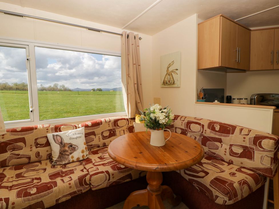 A dining area with a round wooden table and patterned corner seating next to a large window showing a green field at Hollie in Raglan