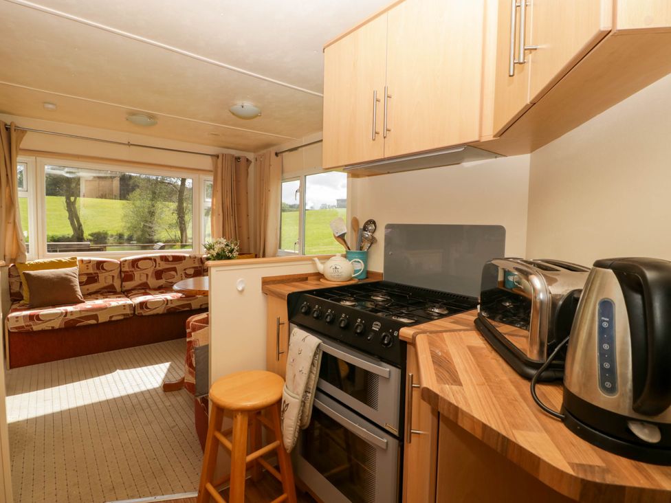 A kitchen area with stove toaster and kettle next to a seating area with couch and table at Hollie in Raglan