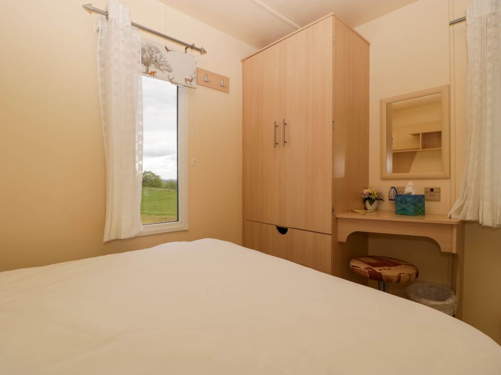 A bedroom with a bed a window with curtains a wooden wardrobe and a dressing table with a stool at Hollie Raglan