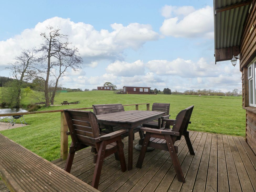 A wooden deck with a table and chairs overlooking a grassy field with cabins and trees at Hollie in Raglan