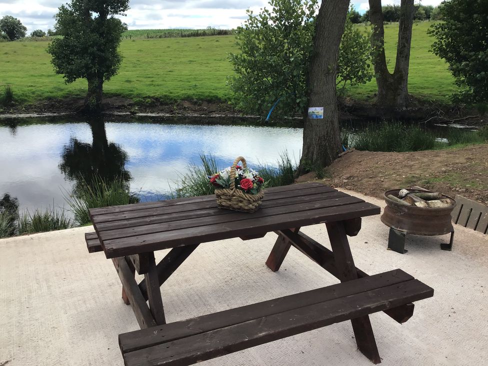 A wooden picnic table with a basket of flowers beside a pond with trees at Hollie in Raglan