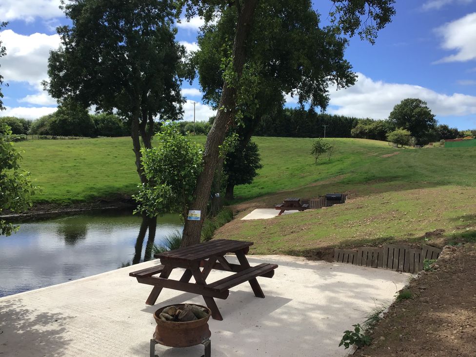 An outdoor area with picnic benches near a pond and grassy field at Hollie in Raglan