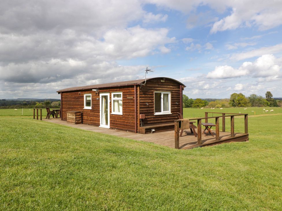 A wooden cabin with a deck and outdoor seating in a grassy field at Poppy in Raglan