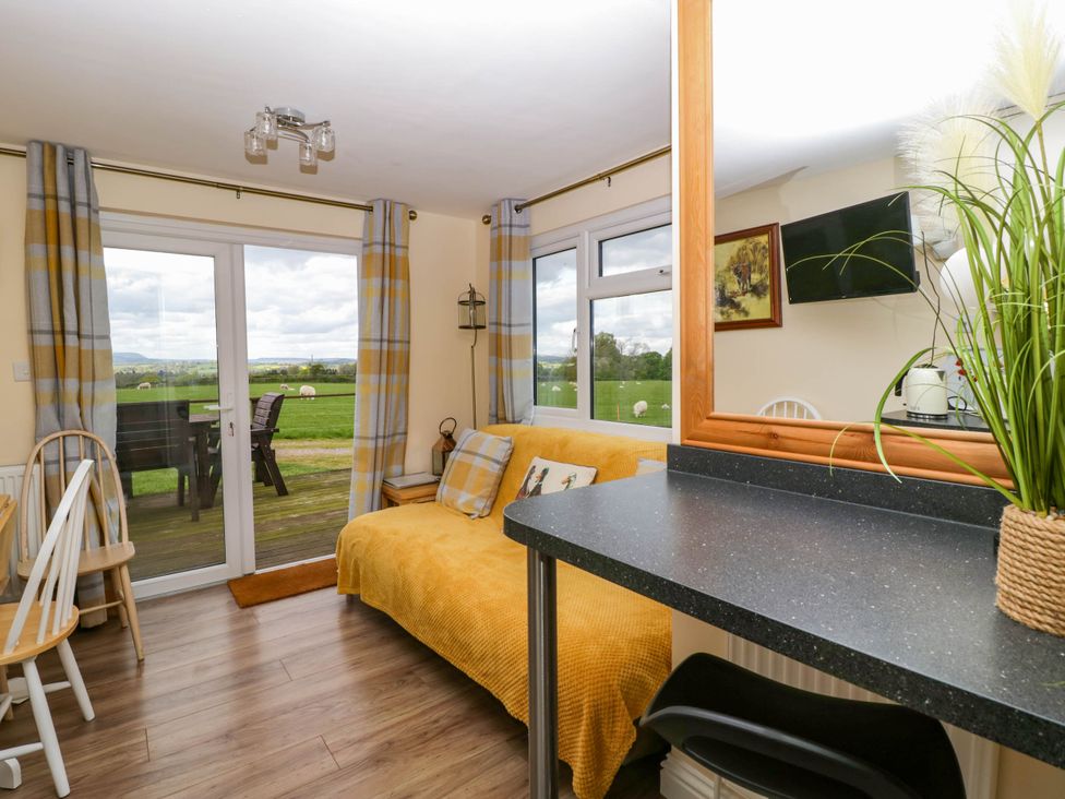 A living room with a yellow throw on the sofa a dining table with chairs and large windows overlooking a green field at Poppy in Raglan