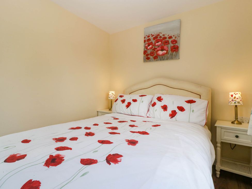 A bedroom with a bed with red flower bedding two bedside tables with lamps and a flower painting on the wall at Poppy in Raglan