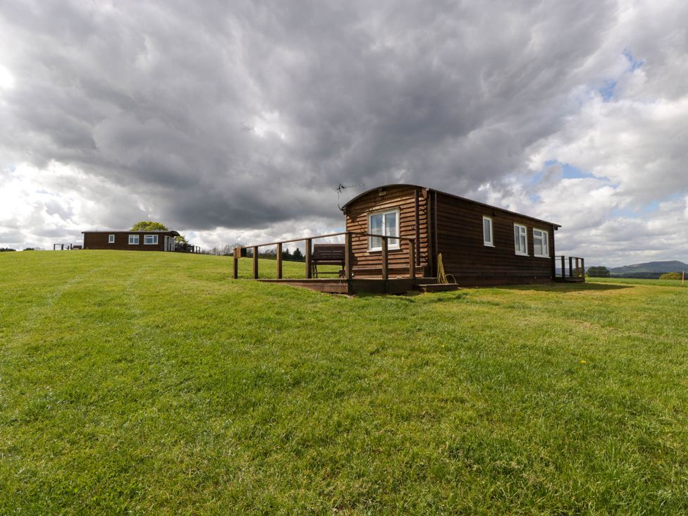 A wooden cabin on a grassy hill under a cloudy sky at Poppy in Raglan