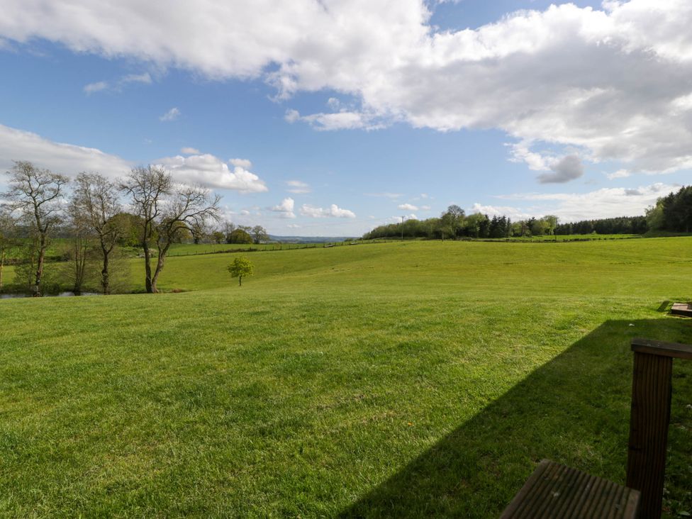 A large grassy field with scattered trees under a partly cloudy sky at Poppy in Raglan