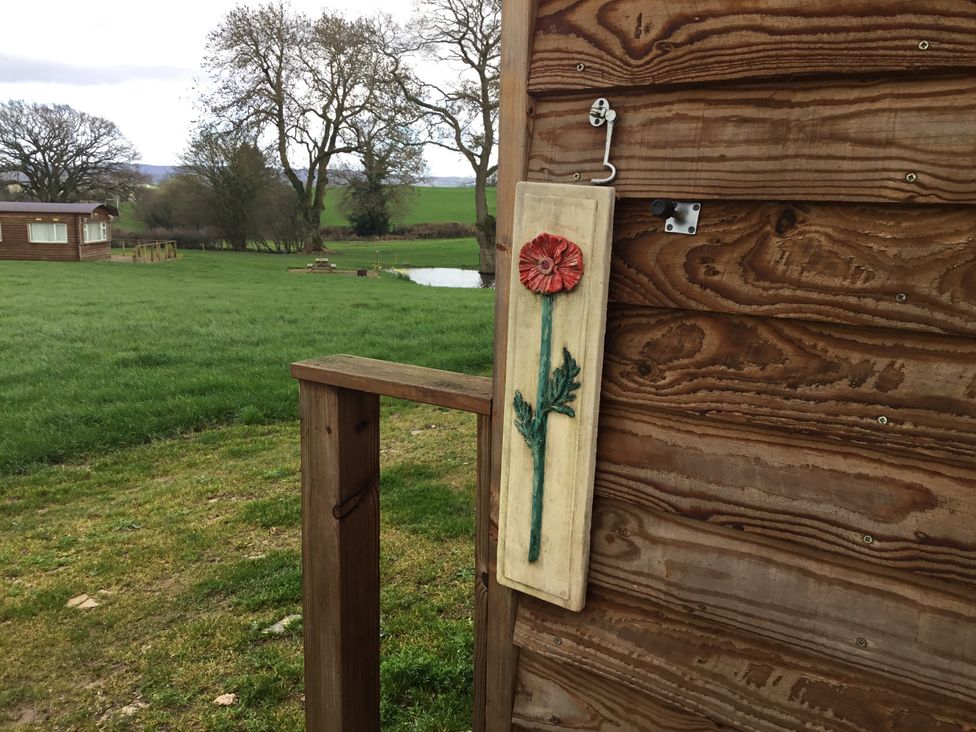 A wooden wall with a painted wooden plaque of a red flower beside a wooden railing with green grass and trees in the background at Poppy in Raglan