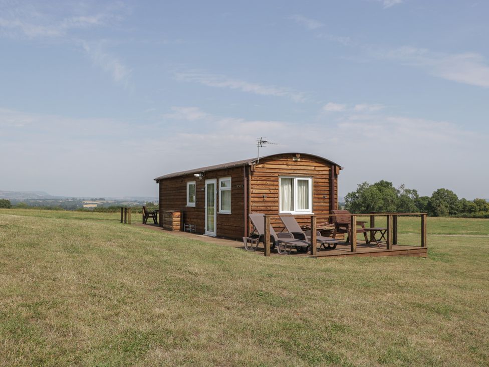 A wooden lodge with a deck in a grass field at Poppy in Raglan