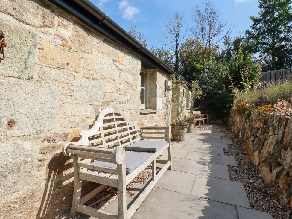 An outdoor space with a bench and stone wall at Stable Loft Watergate Bay