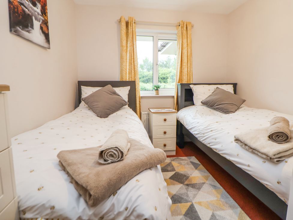 A bedroom with two single beds a window with yellow curtains and a bedside cabinet at 2 Mountain View in Chirk