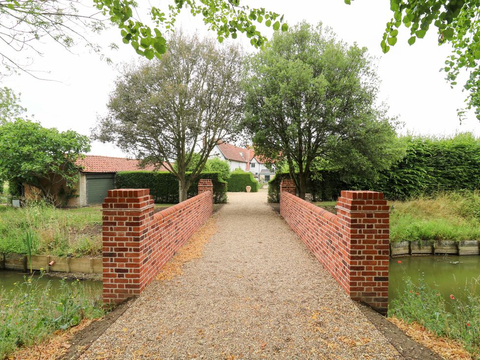 A bridge leading to a house with trees and a garden at Clock Tower in Stowmarket