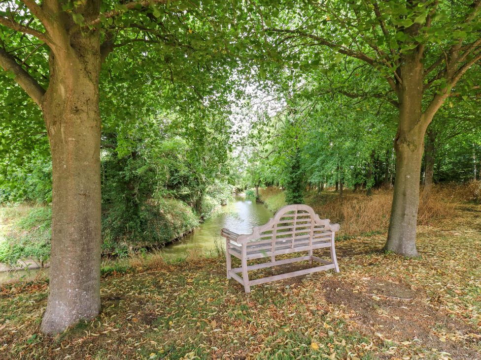 A bench beside a waterway surrounded by trees at Clock Tower in Stowmarket