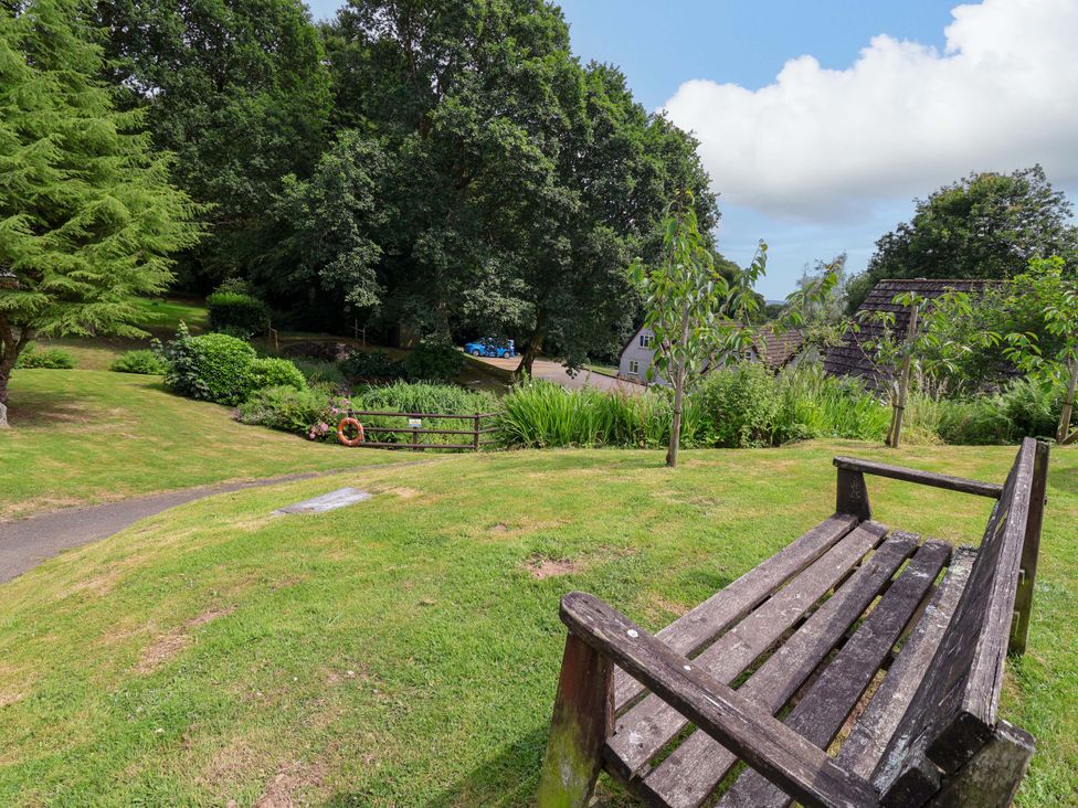 A garden view with a bench and trees at Driftwood - 54 Valley Lodge, St Ann's Chapel, Cornwall