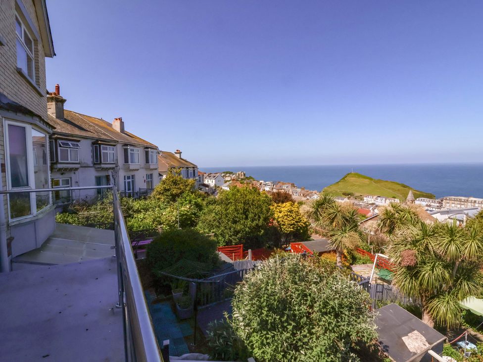 A view of houses and greenery with a hill and ocean in the background at Combe View in Ilfracombe