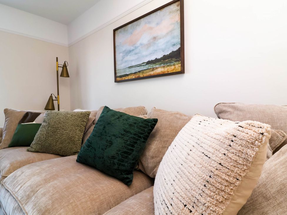 A beige sofa with various cushions and a floor lamp next to a wall with a framed painting at Combe View in Ilfracombe