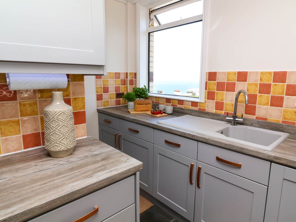A kitchen with grey cabinets orange and yellow tiled backsplash a sink a vase and bread on the counter at Combe View in Ilfracombe
