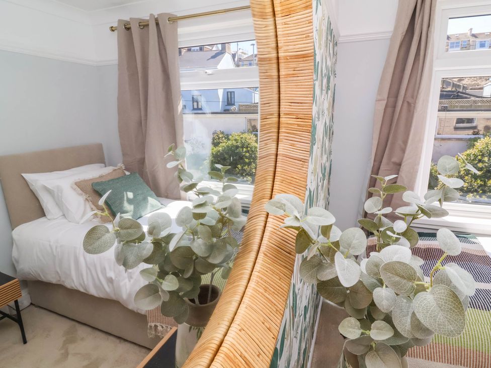A bedroom with a single bed with pillows near two windows and a plant reflected in a curved mirror at Combe View in Ilfracombe