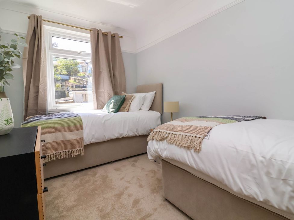 A bedroom with two single beds a window with curtains and a bedside table at Combe View in Ilfracombe