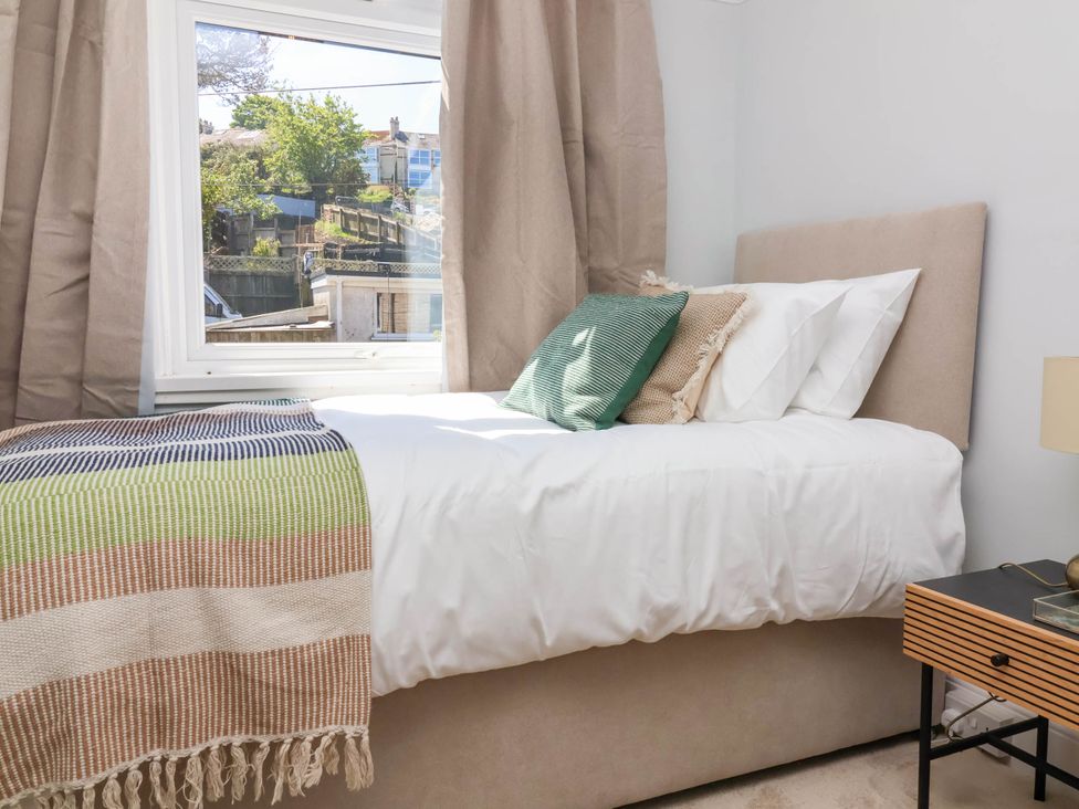 A bedroom with a bed next to a window and a wooden nightstand at Combe View in Ilfracombe