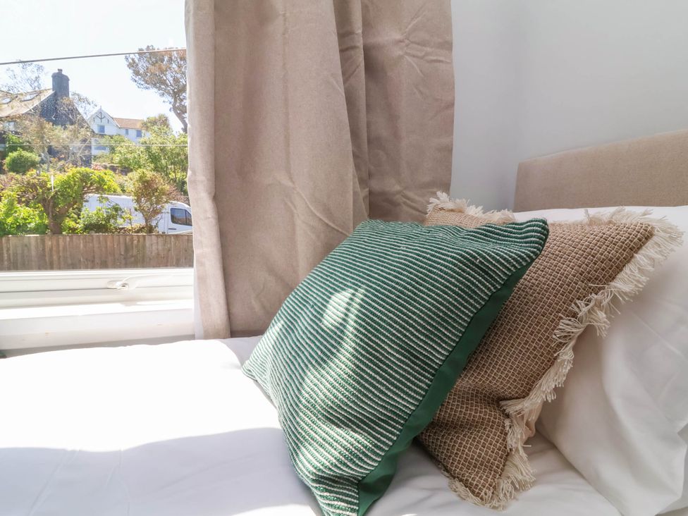 Two pillows on a bed near a window with beige curtains and a view of houses and greenery outside at Combe View in Ilfracombe