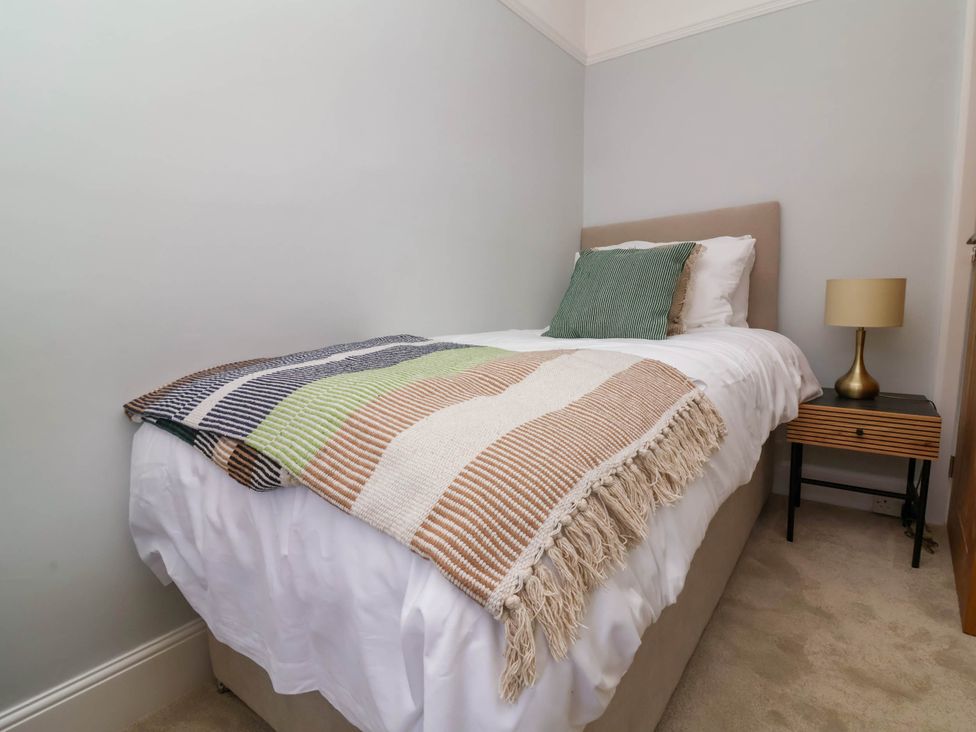 A bedroom with a single bed covered in white linens and a striped blanket with a green pillow next to a bedside table with a lamp at Combe View Ilfracombe