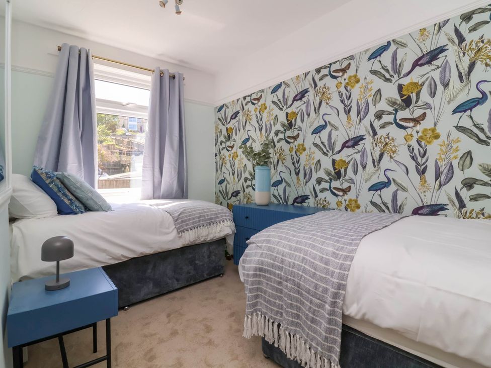 A bedroom with two single beds a blue chest of drawers blue bedside table and floral wallpaper at Combe View in Ilfracombe