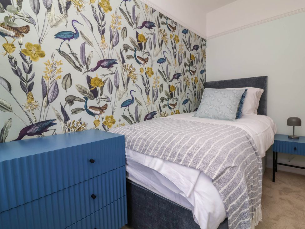 A bedroom with a single bed a blue chest of drawers and floral wallpaper at Combe View in Ilfracombe