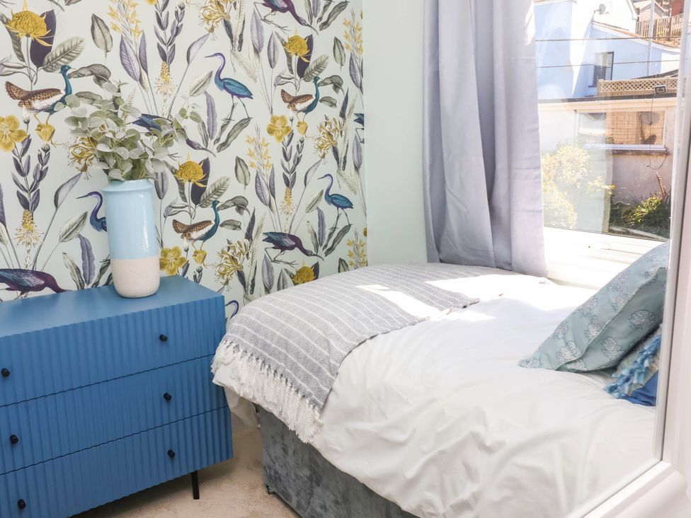 A bedroom with a blue chest of drawers and a bed next to a window with gray curtains at Combe View in Ilfracombe