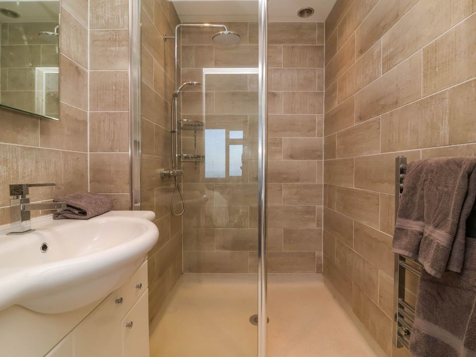A bathroom with a sink and faucet a walk in shower with glass door and brown tiled walls at Combe View in Ilfracombe