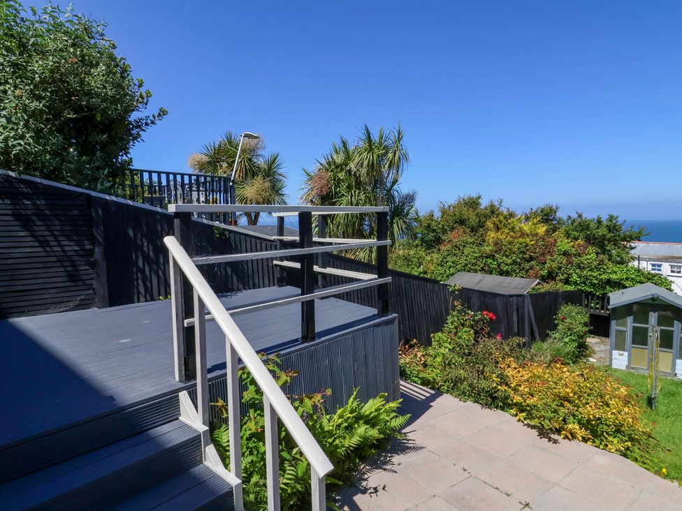 An outdoor garden area with stairs leading to a deck and plants with trees and a shed in the background at Combe View in Ilfracombe